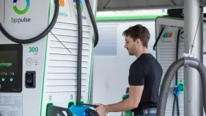 Hombre conectando un coche eléctrico a un cargador rápido BP Pulse de 300 kW en una estación de recarga.